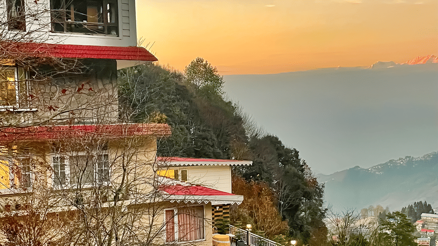 Exterior view of a multi-storey resort building during a golden sunset over the hills | Voyage Rodhi Resort