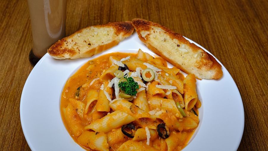 Pasta served in a wide mouth bowl with two pieces of toast and a glass of cold coffee
