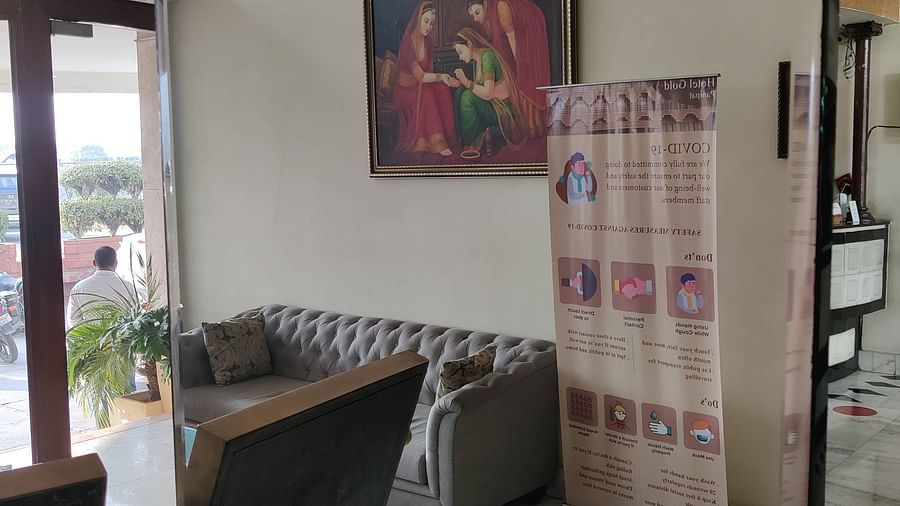 The lobby area of Hotel Gold, Panipat with an elegant grey couch alongside a standee.