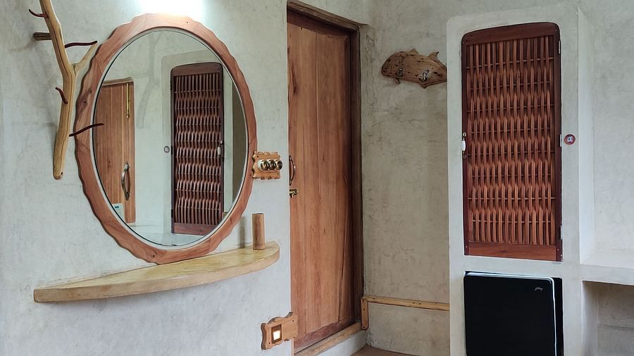 Amberjack-door entrance close up view- cicular mirror wired by wooden strip around it accompanied by a small wooden bar for storage. A singular wardrobe and luggage storage also can be seen.