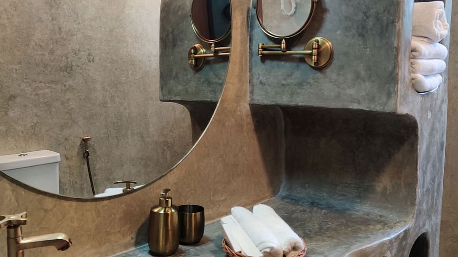 Ocean-washroom circular mirror and a brass coloured basin interior, along with copper painted taps and hand wash liquid dispensers.