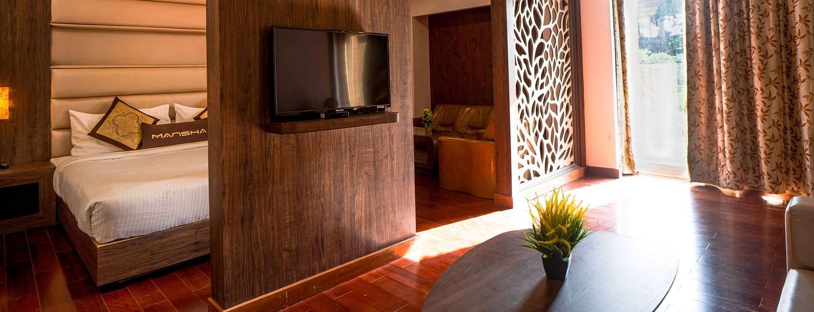 A hotel room interior with a wooden partition separating the sleeping area from a living, featuring warm lighting at Mansha Hotel Regency.