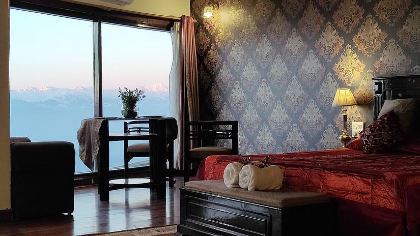 Luxurious room at Hotel Mount View with elegant wallpaper, a rich red bedspread, cosy seating, and large window offering breathtaking mountain views at sunrise.