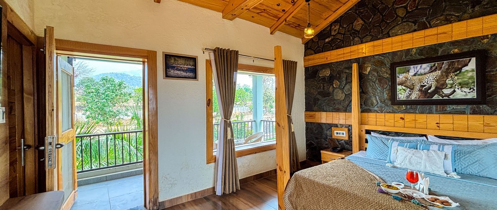 Spacious resort room with wooden ceiling, large windows, and balcony at Corbett Nirvana Resort.