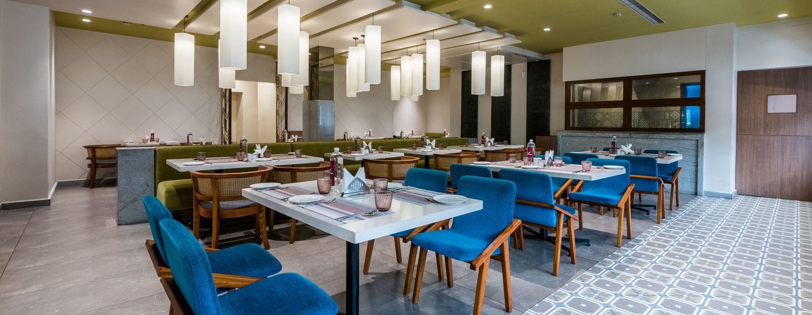A well appointed dining room with vibrant blue chairs and light green walls, illuminated by multiple pendant lights at Shilton Dee Cee.