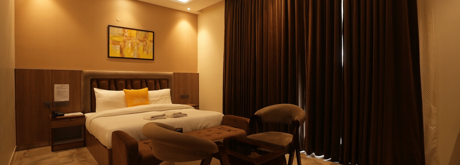 Spacious room with seating area, king size bed, and a ceiling-to-floor curtains at Lime Tree Hotel Near India Expo Mart, Greater Noida.