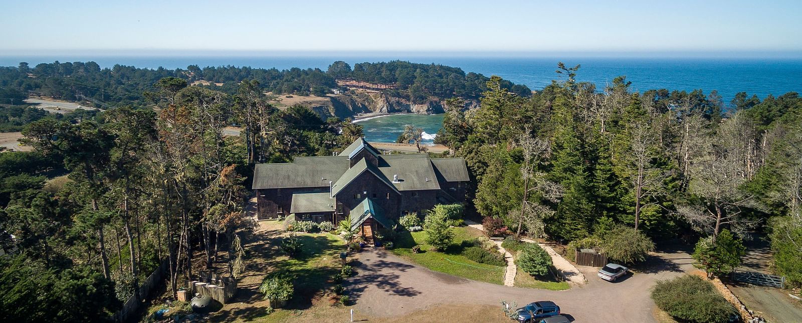 An aerial view of a hotel covered in lush green trees with the Mendocino coast in the background - Brewery Gulch Inn & Spa