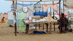 a street market on the beach with a person sitting next to a stand