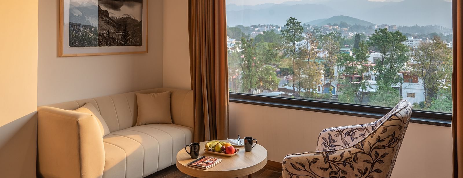 Living area of a suite at Vishranti Hotel, Dehradun Featuring a large window, a sofa, chair and a round table.