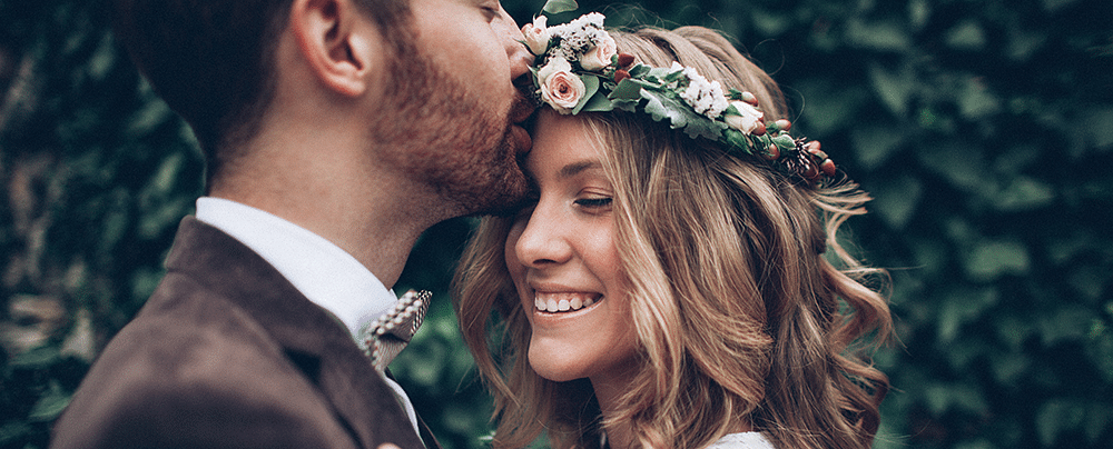 a happy couple dressed in wedding attire with the groom kissing the brides forehead