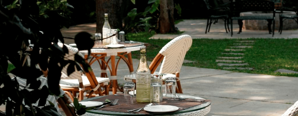 Garden seating area with round tables shaded by trees at Amanvana Spa Resort Coorg, perfect for alfresco meals or tea in Coorg.