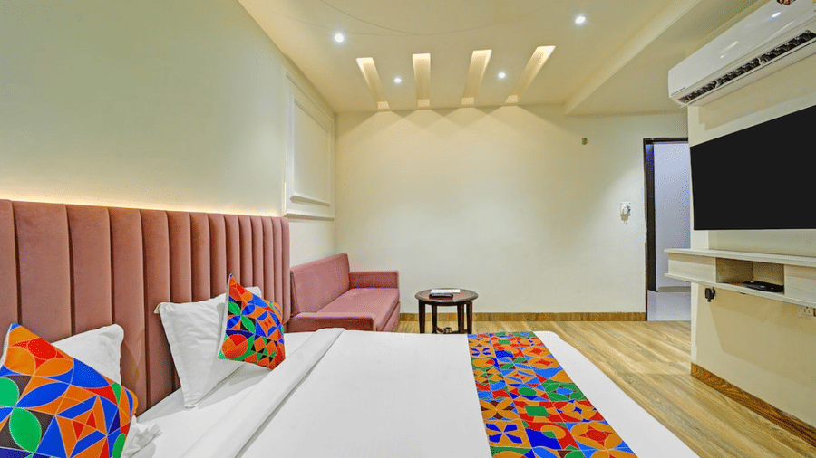 Twin beds with colorful runners, side table, TV unit and ceiling lights in guest room at Hotel Maurya, Bhopal.