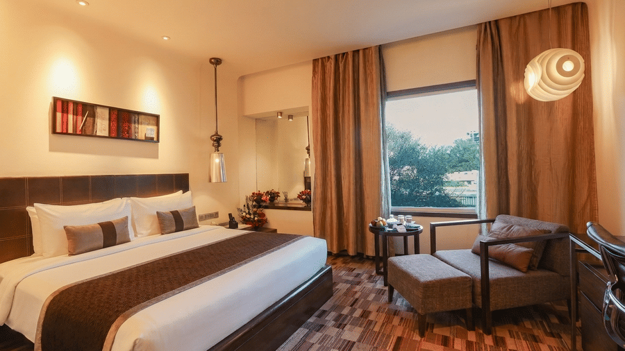 Guest room at Pride Premier Pune featuring a king size bed, seating area and large window with city views.