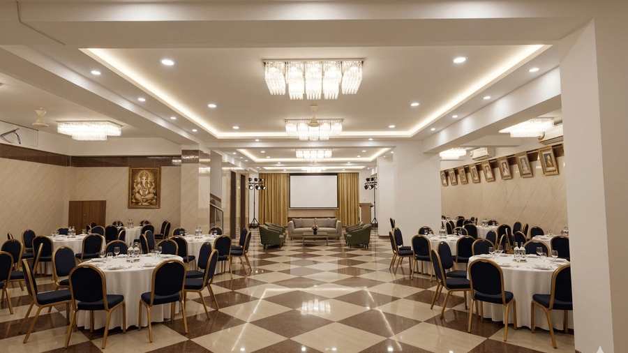 A modern event hall with cluster style seating with round tables covered with white tablecloth and black chairs.