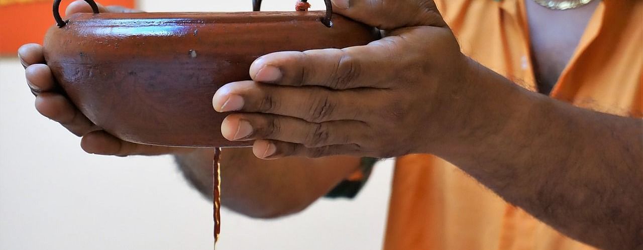a person holding a clay pot with a small hole in the bottom to let the oil flow down through a thread