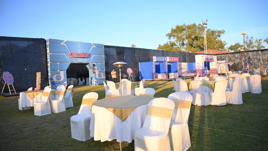 A lawn seating arrangement with round tables, covered chairs, and a stage visible in the background.