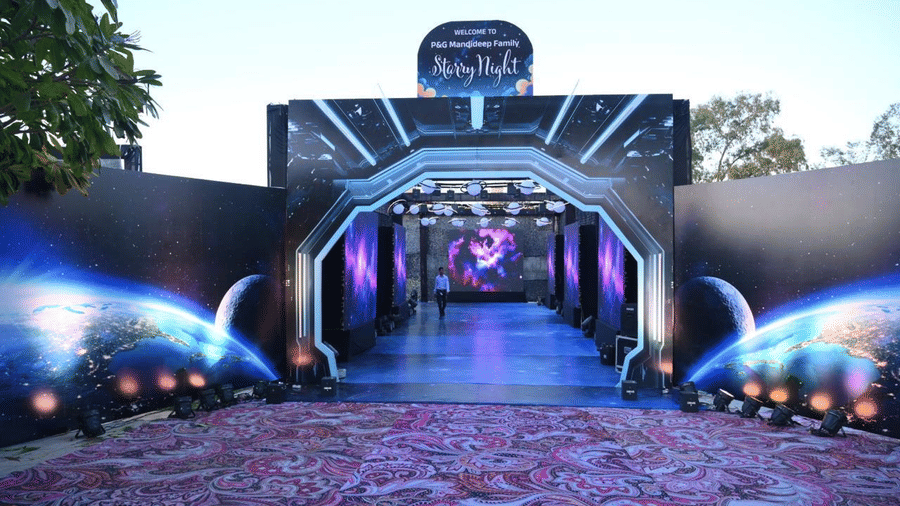 An illuminated tunnel-style event entrance with layered arch frames, lighting effects, and a patterned walkway.