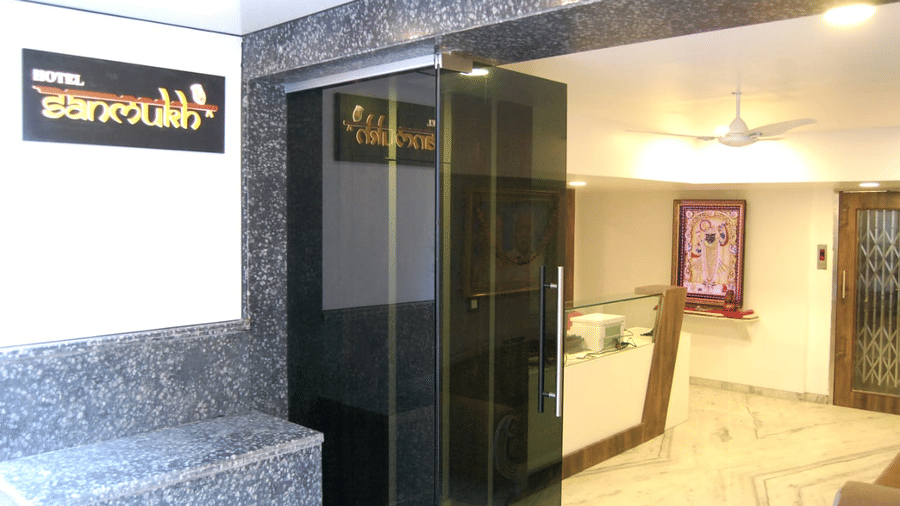 Main entrance of  Adamo Sanmukh with a name tag attached to the wall next to stairs.