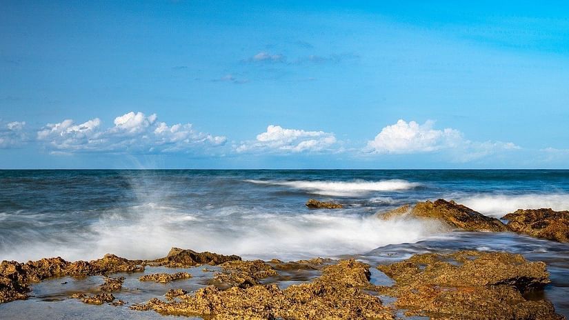 Beach view with waves crashing against small rocks on the shore.