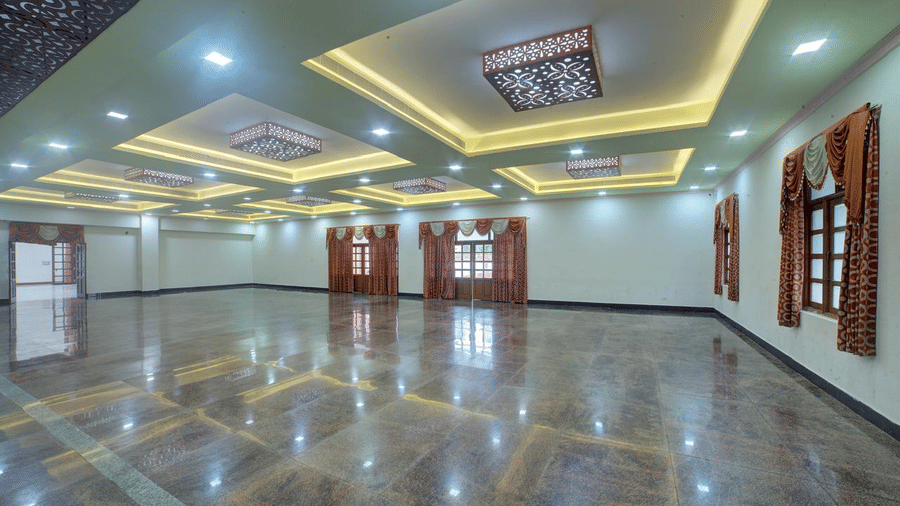 An empty banquet hall featuring a glossy tiled floor, recessed ceiling lights, and windows with brown curtains | Kailash Conventions ECR