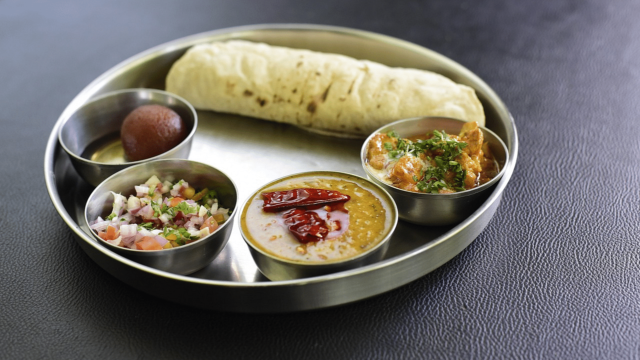 Indian meal with roti, dal, and vegetable dishes on a metal plate.