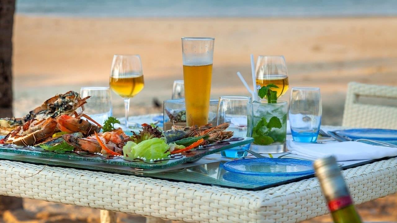 a close up shot of a table with many food items and beverages by the beach - Caravela Beach Resort Goa