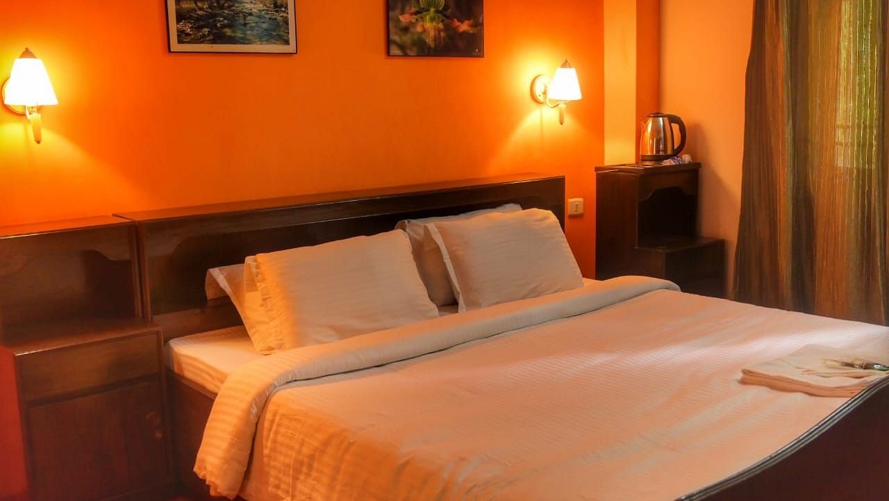 An image of the deluxe room featuring a queen size bed, bed side table, lamps, and painting hung on the wall - Ecotel Chiminda, Pelling