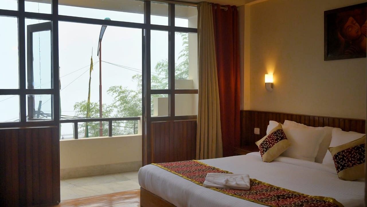 An image of the super deluxe room at Sumitel Chiminda, Pelling featuring a queen size bed, and an expansive door leading to the balcony