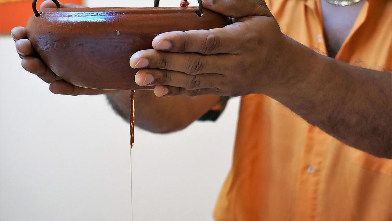 a person holding a clay pot with a small hole in the bottom to let the oil flow down through a thread