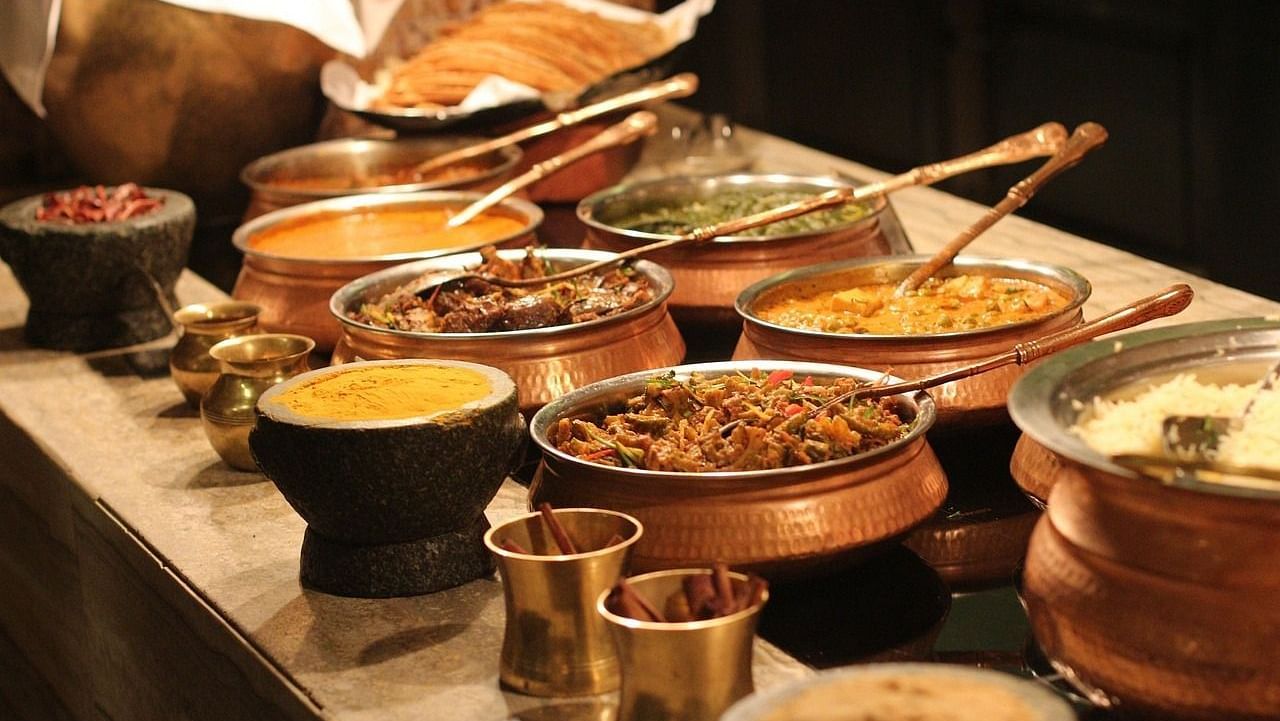 An array of Indian dishes served in traditional brass and stone cookware, featuring a variety of curries, rice, and breads.