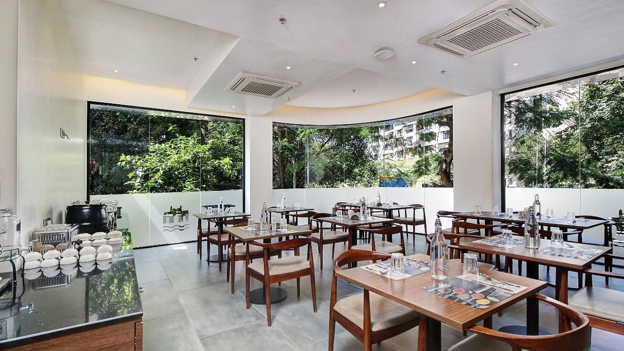 Well lit restaurant area at Hotel Mumbai House, Ghansoli with wooden tables and chairs