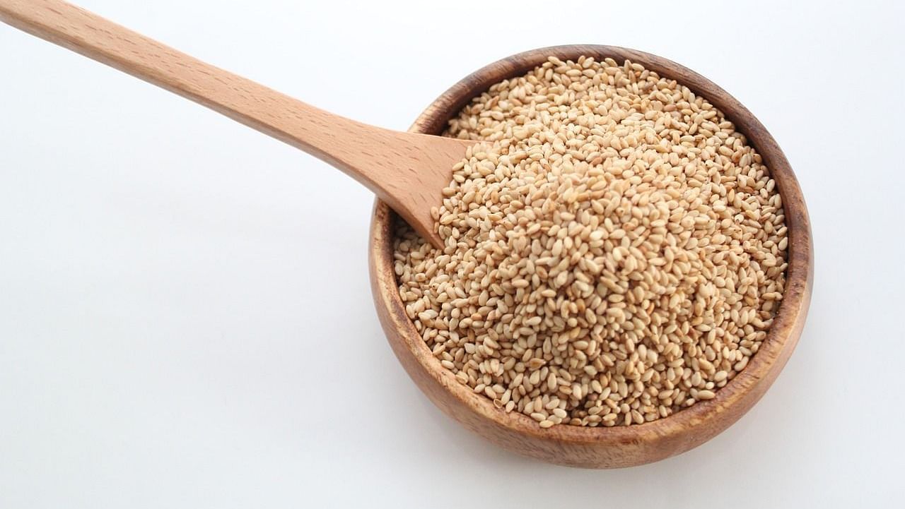 An image of a wooden bowl filled with white sesame seeds, with a spoon placed inside.