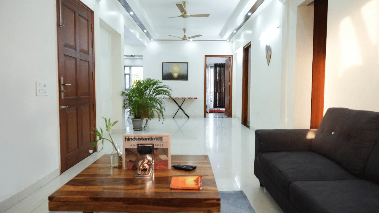Modern hotel lobby lounge featuring a wooden coffee table, a dark grey sofa, indoor potted plants, and a wooden door.