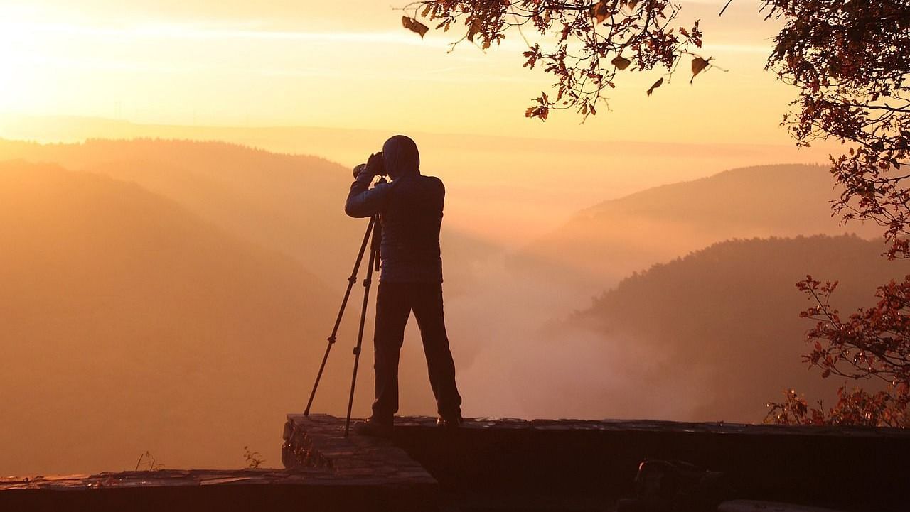 Photographer capturing a scenic sunrise over misty mountains.