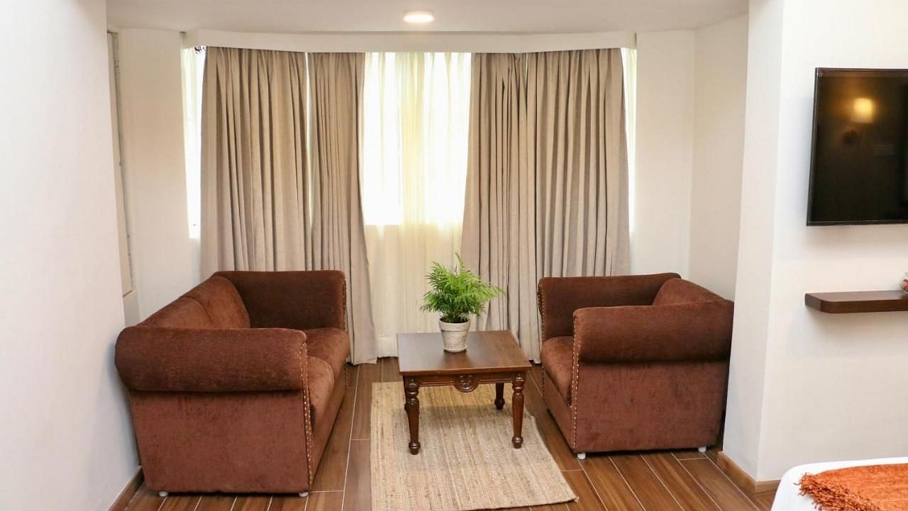 A living room of a Luxury Junior Suite with armchairs, a table, and neutral decor. - Nalapad Hotel Bangalore