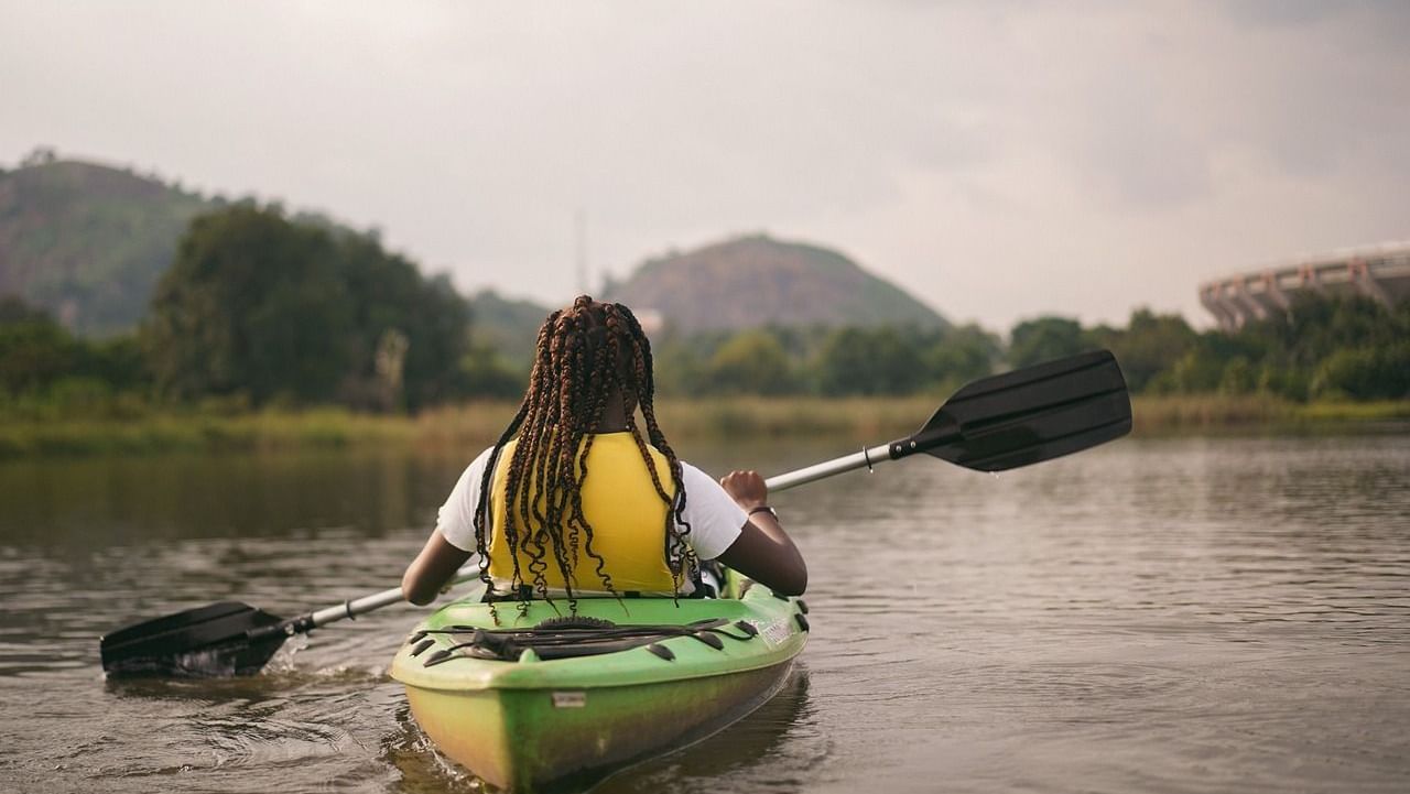 A woman on a kayak, rowing in water with hills and fog surrounded