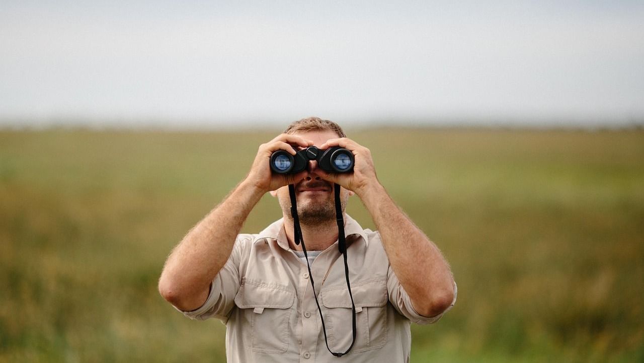 A man in green pastures looking into a binocular
