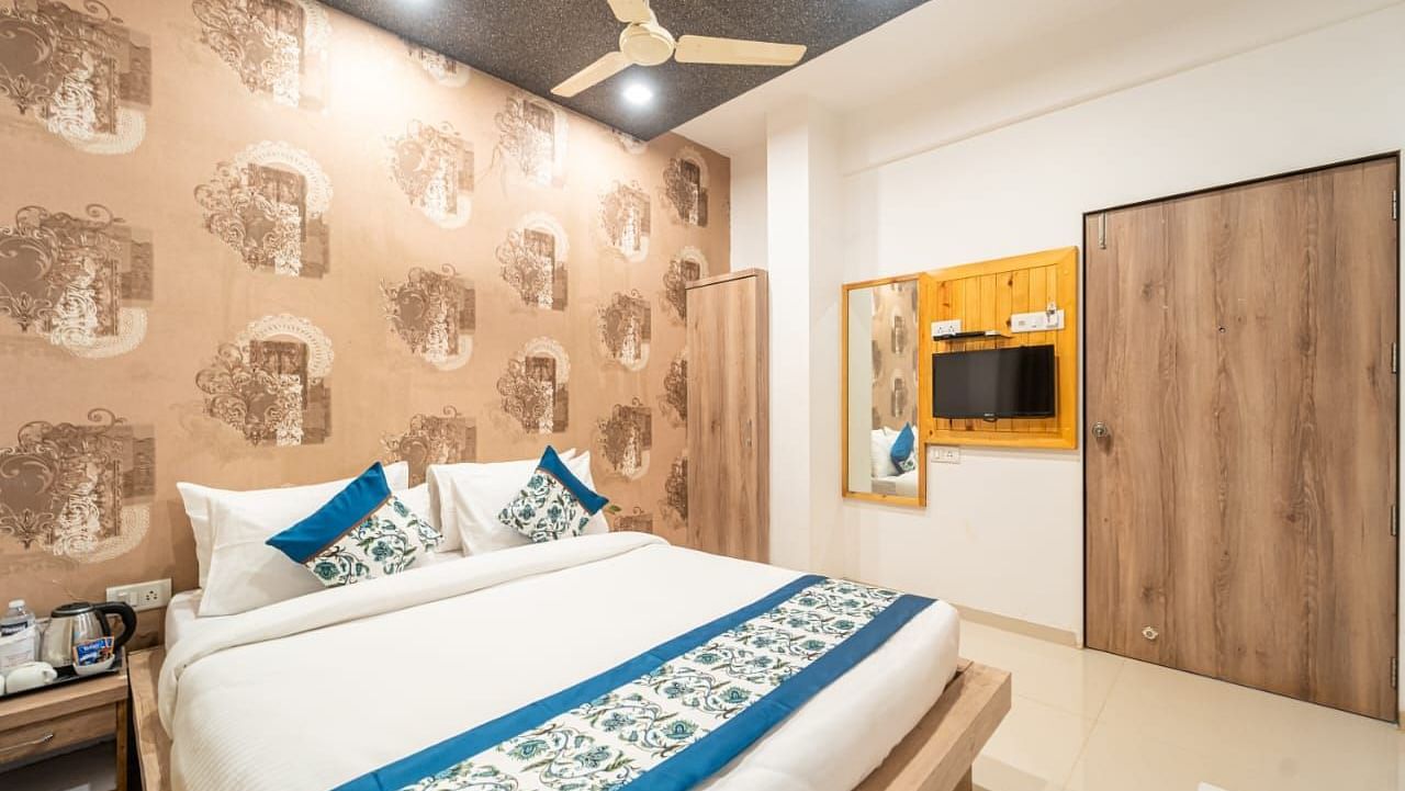 A room featuring a bed with blue and white linens, a patterned wallpaper, a ceiling fan, a television, and a wooden closet. 