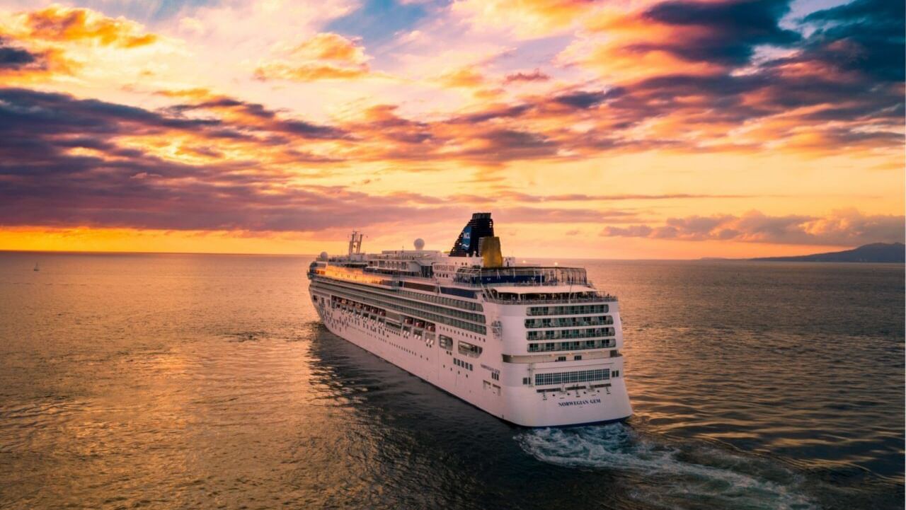 A cruise ship sails through calm waters beneath a vibrant sunset sky.