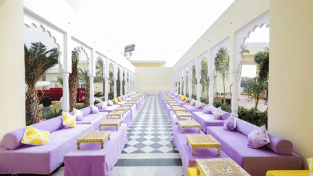 A long corridor with a parallel seating setup and cushions along both sides at Beelwa Palace, Jaipur.