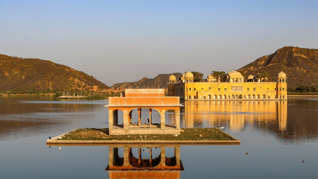Scenic view of Jal Mahal palace surrounded by calm waters and hills at sunrise in Jaipur.