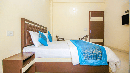 Bedroom of Lime Tree Hotels & Service Apartment Private Limited featuring a wooden headboard, teal bedding, and a wall mounted television.