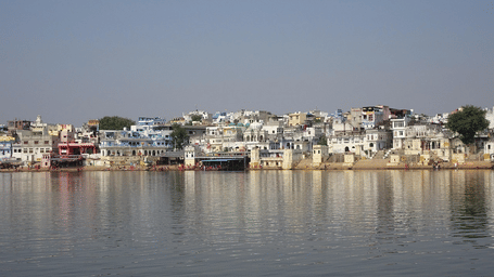A wide shot of a lake reflecting a row of buildings along the shoreline under a clear sky | Ajmer best places to visit