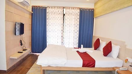 A side view of a spacious room with a large bed. Right opposite to it, there is a wall-mounted TV, and a large window with curtains fully covering it at SeaFort Beach Resort
