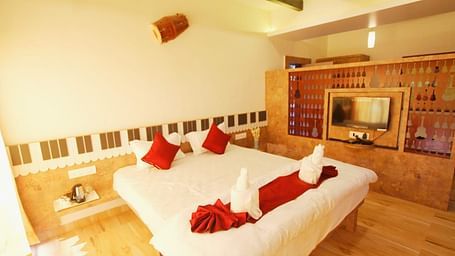 A diagonal view of the room featuring a spacious bed with towels folded in different shapes on it. There is a wooden table with a wall-mounted television at SeaFort Beach Resort