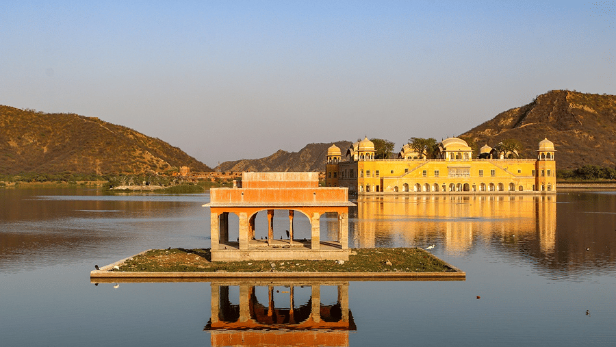 Jal Mahal, a yellow stone palace on the calm water of Man Sagar Lake with hills behind it