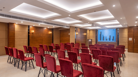 Mid-size conference room with rows of red chairs facing a presentation screen.