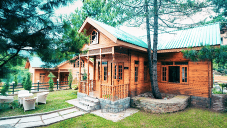 Exterior of a wooden cottage at Dawat e Drung by FrozenFall Resort, Drung, Tangmarg, surrounded by a lawn area, stone paths and tall trees.