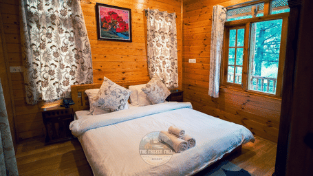 1BHK Villa bedroom at Dawat e Drung by FrozenFall Resort, Drung, Tangmarg, featuring a double bed with folded towels, window curtains and wooden walls.