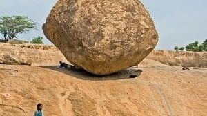A large boulder on a slope with a woman and a bird in the foreground.